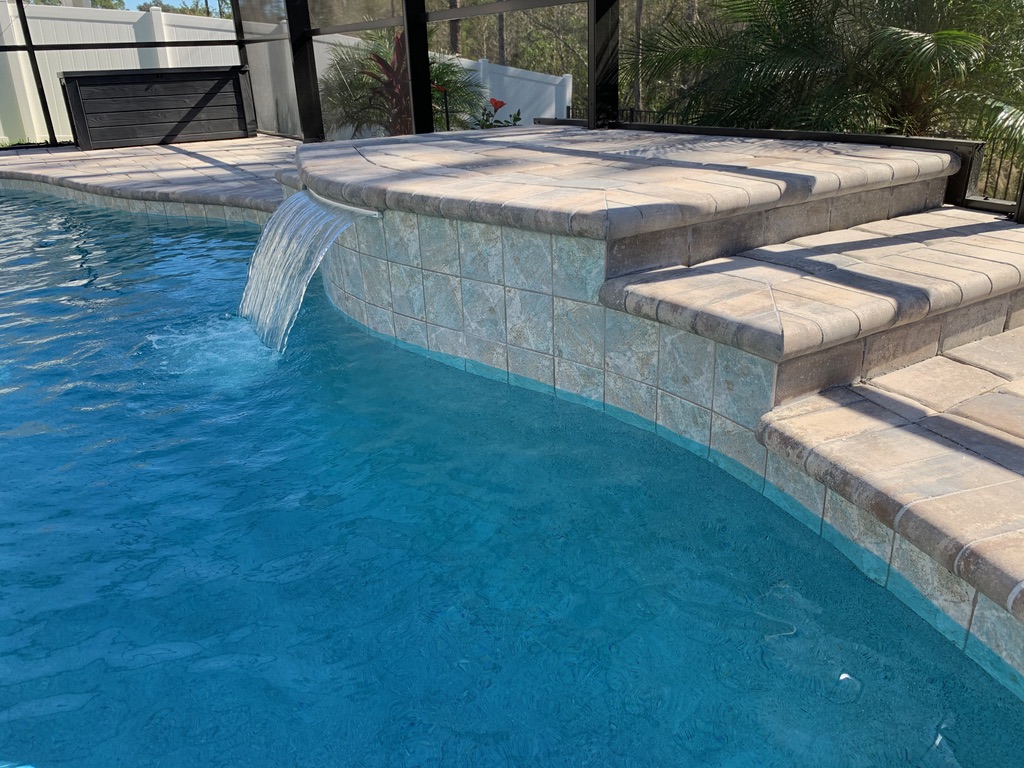 Waterfall feature cascading into a pool, showcasing elegant stonework and blue water, part of Breakwater Construction's waterfall project collection.