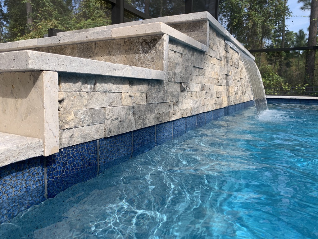 Waterfall feature cascading into a blue-tiled pool, showcasing stonework and water design by Breakwater Construction.