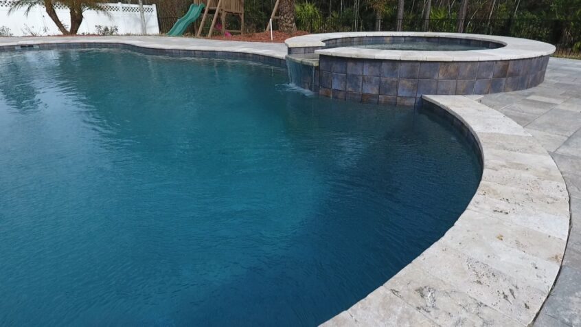 Luxury pool design featuring a curved edge, spa area, and clear blue water, showcasing the SmithB_Spa project by Breakwater Construction.