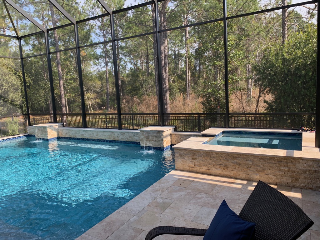 Water feature with waterfall cascading into a pool area, surrounded by a screened enclosure and lush greenery, showcasing Breakwater Construction's design expertise in outdoor spaces.