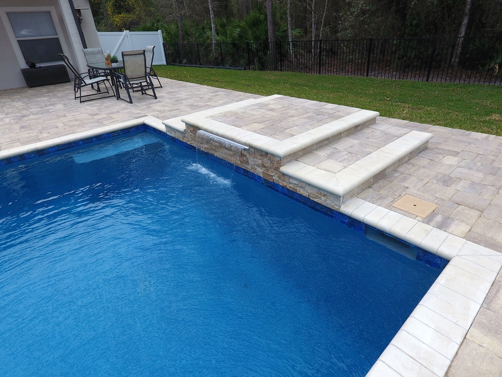 Pool area featuring a stone waterfall feature, blue water, and surrounding patio with seating, showcasing Breakwater Construction's waterfall design and pool integration.