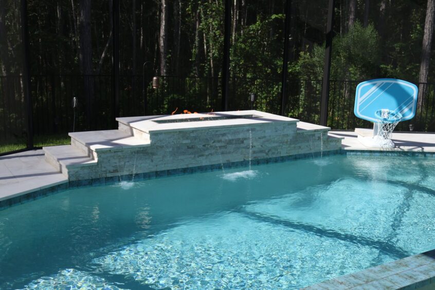 Linear gas fire feature with lava rock and three sheer descent waterfalls spilling into the geometric Backyard Retreat Pool in St. Augustine, Florida
