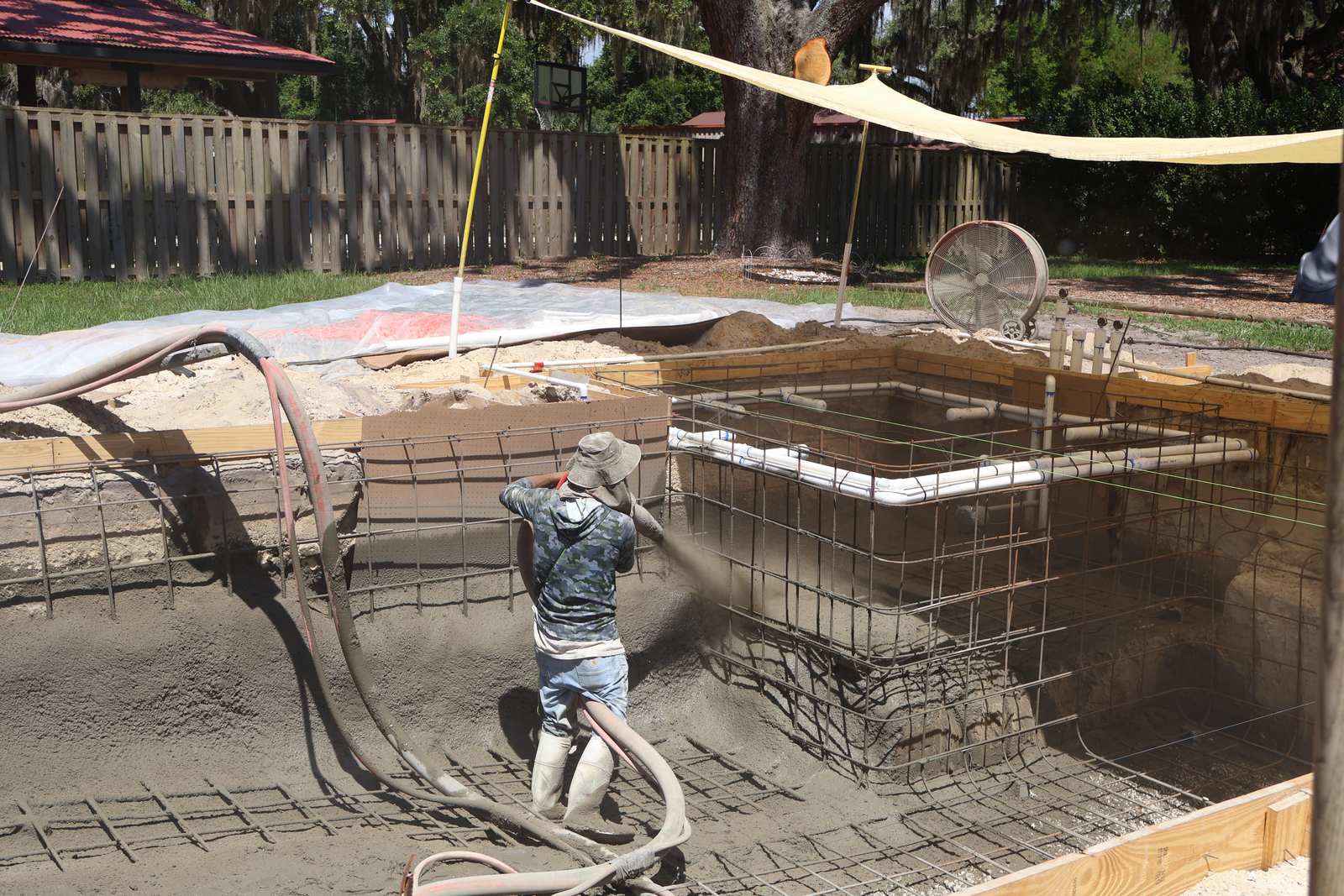 A crew member spraying gunite over steel reinforcement to form the structural shell of a pool